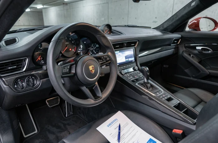 Intérieur cockpit d'une Porsche 911 avec document d'assurance auto posé sur le siège passager en cuir